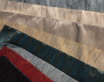 Op de afbeelding: Een assortiment van getextureerde stofstalen in verschillende kleuren, waaronder crème, blauw, goud, teal, rood en zwart. De stoffen hebben een subtiel, verticaal streepjespatroon. De stalen zijn in een waaier gerangschikt, met de verschillende kleuropties.