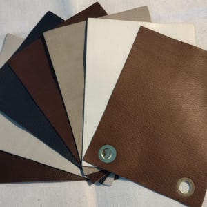 May include: A selection of leather swatches in a range of neutral tones, such as brown, beige, and navy. The swatches are fanned out, with some featuring metal eyelets. The leather has a textured appearance.
