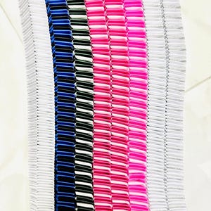 以下が含まれることがあります： さまざまな色のプリーツ生地が縦に並んだクローズアップ。白、青、黒、ピンク、シルバーなどの色が含まれています。生地はアコーディオンのような質感で、各プリーツがはっきりと定義されています。