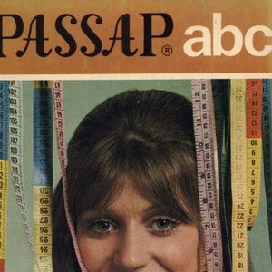 May include: A woman with long brown hair is smiling. She is wearing a white shirt and has a measuring tape around her neck. The measuring tape has numbers on it and is in different colors. The background is a light brown color with the text "PASSAP abc" printed on it.