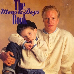 May include: A father and son wearing cream colored sweaters and blue jeans. The father is holding the son on his lap. The text "The Mens & Boys Book" is at the top of the image. The text "Knitmaster Creative Kone Apply Aneto Black Pack" is at the bottom of the image.