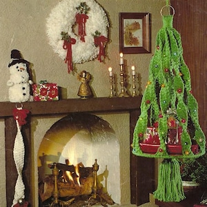 May include: A crochet pattern for a Christmas tree, wreath, and stocking. The pattern is called "Maxi Christmas" and uses Maxi-Cord 8 ply yarn. The image shows a green crochet Christmas tree hanging from the ceiling, a white crochet wreath on the wall, and a white crochet stocking hanging from a fireplace mantel.