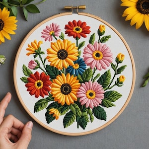 May include: A colorful floral embroidery hoop featuring a bouquet of embroidered flowers in shades of yellow, orange, pink, and blue. The flowers are surrounded by green leaves, all set against a white fabric background within a wooden hoop.