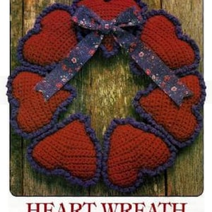 May include: A crocheted heart wreath with a red and purple color scheme. The wreath is decorated with a blue ribbon with white floral print.
