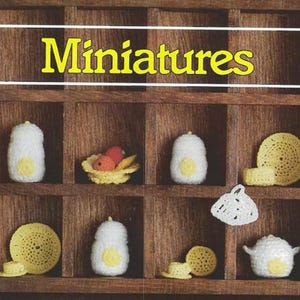 Könnte beinhalten: Ein Holzregal mit dem Wort "Miniaturen" oben. Das Regal ist in 10 Fächer unterteilt. Jedes Fach enthält einen gehäkelten Artikel, darunter eine Teekanne, ein Teller, eine Schüssel und eine Tasse.