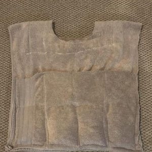 May include: A grey, rectangular heating pad with a curved neck cutout. The pad is sectioned and has a textured surface. Designed for therapeutic use, it measures approximately 50 cm x 40 cm.