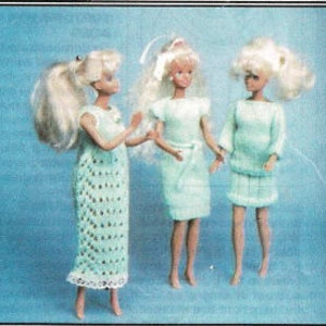 Puede incluir: Tres muñecas rubias vestidas con trajes verde claro hechos a mano. La muñeca de la izquierda lleva un vestido largo de tejido abierto. La muñeca del centro lleva un vestido corto con cinturón. La muñeca de la derecha lleva un jersey y una falda.