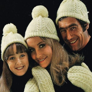 May include: A family of three wearing matching knitted hats and mittens. The hats are white with a cable knit pattern and have a white pom-pom on top. The mittens are also white with a cable knit pattern.