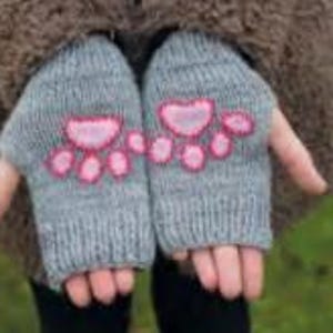 May include: Gray knitted fingerless gloves with pink paw print designs. The gloves are made of a soft, textured yarn and are designed to keep hands warm while allowing for finger movement. The paw prints are embroidered.