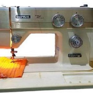 May include: A vintage cream and gold EMPISAL sewing machine. The machine has several dials and is actively sewing orange fabric. The machine sits on a white base with a red accent.