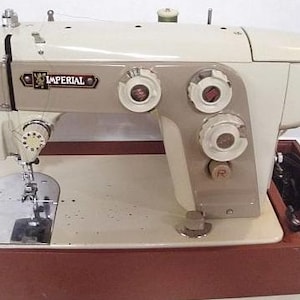 May include: A vintage white Imperial sewing machine with a brown wooden case. The machine has multiple dials and a foot pedal.