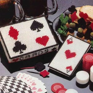 Pode incluir: Um conjunto de artesanato temático de cartas de jogar em branco e vermelho. O conjunto inclui uma caixa de cartas, um único cartão de jogar e um baralho de cartas. A caixa de cartas tem a palavra "CARDS" nela. O único cartão de jogar é um ás de paus. O baralho de cartas está virado para baixo.