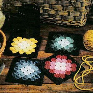 May include: Four crocheted squares with different colored flower designs. The squares are yellow, blue, pink, and green. The squares are on a wooden surface.
