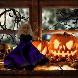 Könnte beinhalten: Eine Puppe in einem lila Kleid mit schwarzem Saum steht vor einem Fenster mit zwei Jack-o'-Lantern. Das Fenster befindet sich hinter einer Holzbrüstung.