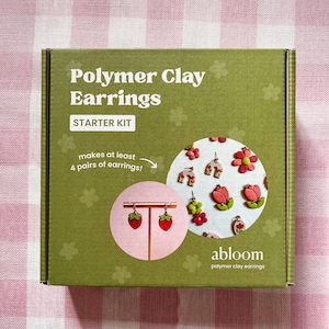 May include: A green box labeled "Polymer Clay Earrings STARTER KIT" with a pink and white gingham background. The box features a strawberry earring design and states it makes at least 4 pairs of earrings. The brand name "abloom" is also visible.