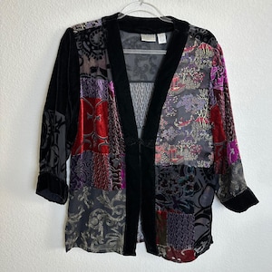 May include: A patchwork jacket with a black velvet collar and trim. The jacket features a variety of patterned fabrics in shades of red, purple, gray, and black. The sleeves are three-quarter length.