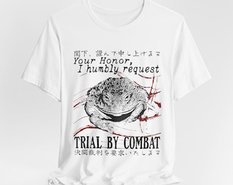 Op de afbeelding: Een wit t-shirt met korte mouwen en een zwart-witte illustratie van een pad. De afbeelding bevat de tekst "Your Honor, I humbly request TRIAL BY COMBAT" samen met Japanse karakters boven en onder de illustratie van de pad.