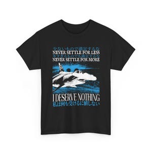 May include: A black short-sleeve t-shirt featuring a graphic of a hammerhead shark in blue and white. The text reads: NEVER SETTLE FOR LESS, NEVER SETTLE FOR MORE, I DESERVE NOTHING, along with Japanese characters above and below the shark graphic.