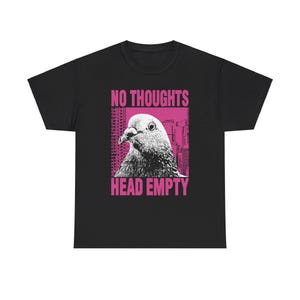 Può includere: Maglietta nera con una grafica rosa di un piccione con il testo "NO THOUGHTS HEAD EMPTY"