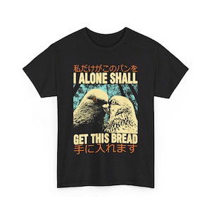 Op de afbeelding: Zwart T-shirt met een afbeelding van twee duiven die elkaar aankijken. De tekst "I alone shall get this bread" is in oranje en wit gedrukt. De Japanse tekst "私だけがこのパンを手に入れます" is in zwart gedrukt.