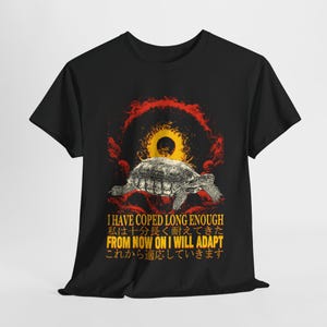 May include: Black t-shirt featuring a graphic of a tortoise walking towards a red and yellow sun. The text "I HAVE COPED LONG ENOUGH 私は十分長く耐えてきた FROM NOW ON I WILL ADAPT これから適応していきます" is printed on the shirt.