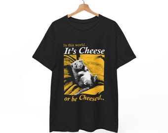 Op de afbeelding: Zwart T-shirt met een gele afbeelding van een rat die op een gele deken ligt. De tekst "In this world... It's Cheese or be Cheesed..." staat op het shirt gedrukt.