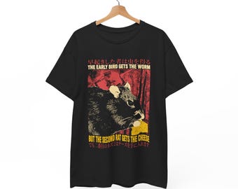 Pode incluir: Camiseta preta com um gráfico de um rato comendo queijo. O texto na camiseta diz "The early bird gets the worm, but the second rat gets the cheese." em inglês e japonês.