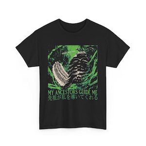 May include: Black t-shirt with a green and white graphic of a large insect-like creature. The text "MY ANCESTORS GUIDE ME" and Japanese text are printed below the graphic. The shirt is made of a soft material.
