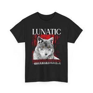 May include: Black t-shirt featuring a wolf illustration with yellow eyes. The word "LUNATIC" is above the wolf, with the phrase "COMMON DECENCY IS A THING OF THE PAST" and Japanese text below. The design is in white and red.