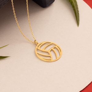 May include: A gold necklace with a volleyball pendant. The pendant is a cut-out design of a volleyball.