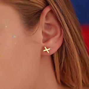 Puede incluir: Primer plano de la cara de una persona con pendientes de cruz de oro. La persona tiene el pelo castaño claro y lleva maquillaje.