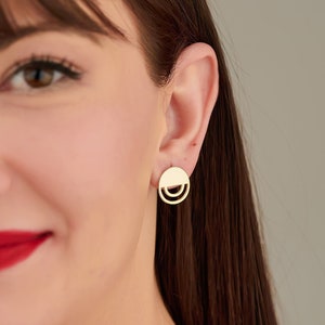 May include: A close-up of a woman's face wearing a pair of gold earrings. The earrings are circular with a double-layered design.
