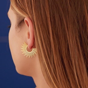 Peut inclure: Boucles d'oreilles cr&eacute;oles en forme de soleil dor&eacute;es. Les boucles d'oreilles sont en m&eacute;tal fin et ont un design d&eacute;licat en forme de soleil.