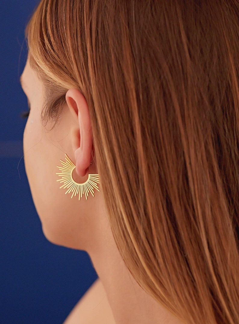 Peut inclure: Boucles d'oreilles cr&eacute;oles en forme de soleil dor&eacute;es. Les boucles d'oreilles sont en m&eacute;tal fin et ont un design d&eacute;licat en forme de soleil.