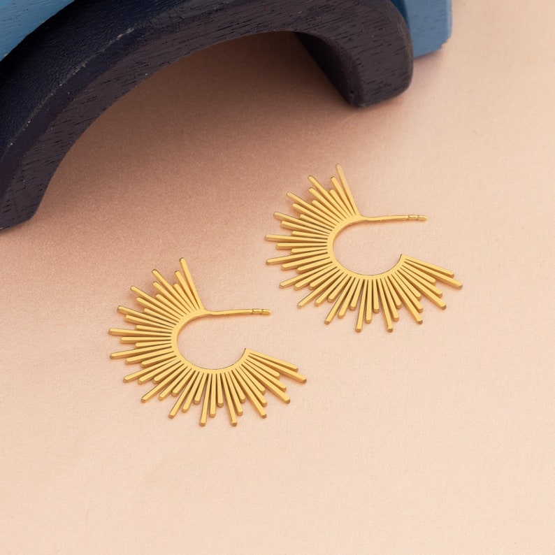 Peut inclure: Une paire de boucles d'oreilles cr&eacute;oles dor&eacute;es avec un motif soleil. Les boucles d'oreilles sont en m&eacute;tal et ont une finition brillante.