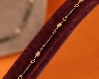 Puede incluir: Un delicado collar de cadena dorada con pequeñas perlas redondas de color blanco roto. La cadena está hecha de metal fino texturizado y tiene un diseño sencillo.