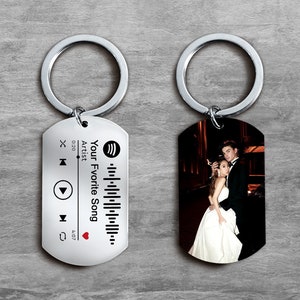 May include: Two silver keychains with a black and white photo of a couple on one keychain and a silver tag with a Spotify logo, a barcode, and the text "Your Favorite Song" on the other keychain.