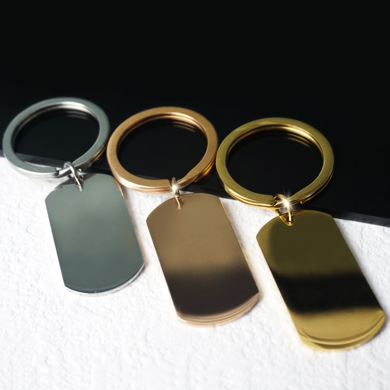 Puede incluir: Tres llaveros con etiquetas met&aacute;licas en blanco. Los llaveros son plateados, dorados y de oro rosa. Las etiquetas son rectangulares y tienen un acabado liso y pulido.