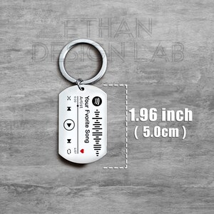 Puede incluir: Un llavero plateado con un dise&ntilde;o en blanco y negro que se asemeja a un reproductor de m&uacute;sica. El llavero mide 1,96 pulgadas (5,0 cm) de largo y presenta un logotipo de Spotify, botones de reproducci&oacute;n y pausa, y el texto "Your Favorite Song".