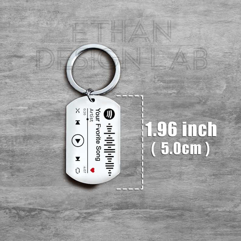 Puede incluir: Un llavero plateado con un dise&ntilde;o en blanco y negro que se asemeja a un reproductor de m&uacute;sica. El llavero mide 1,96 pulgadas (5,0 cm) de largo y presenta un logotipo de Spotify, botones de reproducci&oacute;n y pausa, y el texto "Your Favorite Song".