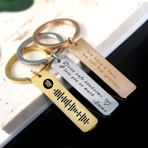 May include: Three gold, silver, and rose gold keychains with engraved messages. The gold keychain has a music note and a barcode. The silver keychain says "Drive safe handsome, I love you so much - Emma". The rose gold keychain says "We have a hero we call him grandpa."