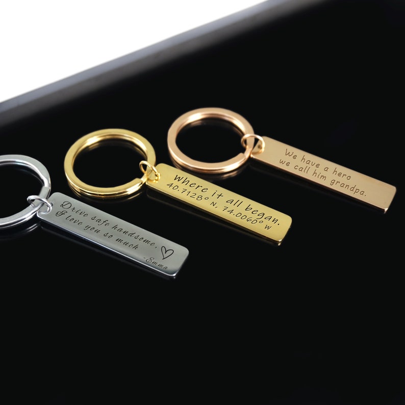 May include: Three silver, gold, and rose gold keychains with engraved messages. The silver keychain says "Drive safe handsome. I love you so much -Emma". The gold keychain says "Where it all began. 40.7128&deg; N, 74.0060&deg; W". The rose gold keychain says "We have a hero we call him grandpa."