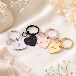 May include: Four metal heart-shaped keyrings in silver, black, rose gold, and gold tones. Each keyring features a split ring, a small heart charm, and a larger heart pendant engraved with the words Hope or Faith Grows Here in script.