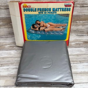 May include: A folded, silver-colored Double French Mattress with 36 pockets, in its original box. The box features an image of two people relaxing on the mattress in a pool. The box reads "SUNCO Double French Mattress".