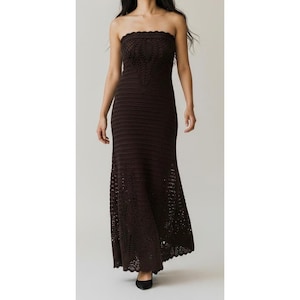 May include: A dark brown, strapless, floor-length dress. The bodice features a textured, patterned design, while the skirt has a horizontal ribbed pattern that flares out at the bottom. The hemline has a scalloped edge.