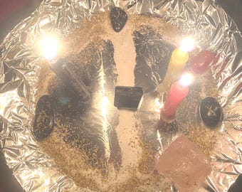 May include: A ritual setup on a silver foil-lined surface. The arrangement includes lit candles in yellow and red, crystals, and small black stones. The scene is illuminated by the candle flames, creating a mystical ambiance.