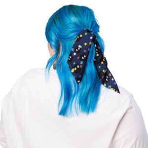 May include: A blue hair scrunchie with a black and white print of a cartoon character with multiple eyes. The scrunchie is tied in a bow around a person's hair.