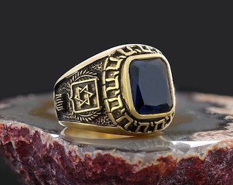 Op de afbeelding: Een gouden ring met een blauwe edelsteen en een Davidster-ontwerp. De ring ligt op een bruin-witte agaat-steen.
