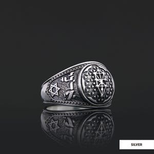 Op de afbeelding: Een zilveren ring met een gedetailleerd ontwerp met een Davidster, Hebreeuwse tekst en een geometrisch patroon. De ring ligt op een zwarte achtergrond.