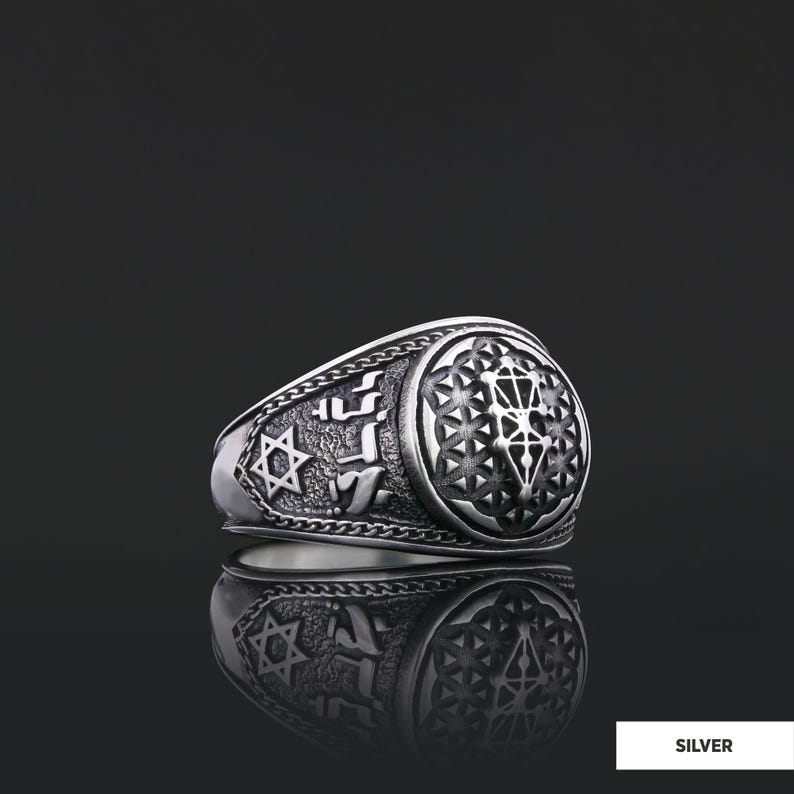 Op de afbeelding: Een zilveren ring met een gedetailleerd ontwerp met een Davidster, Hebreeuwse tekst en een geometrisch patroon. De ring ligt op een zwarte achtergrond.
